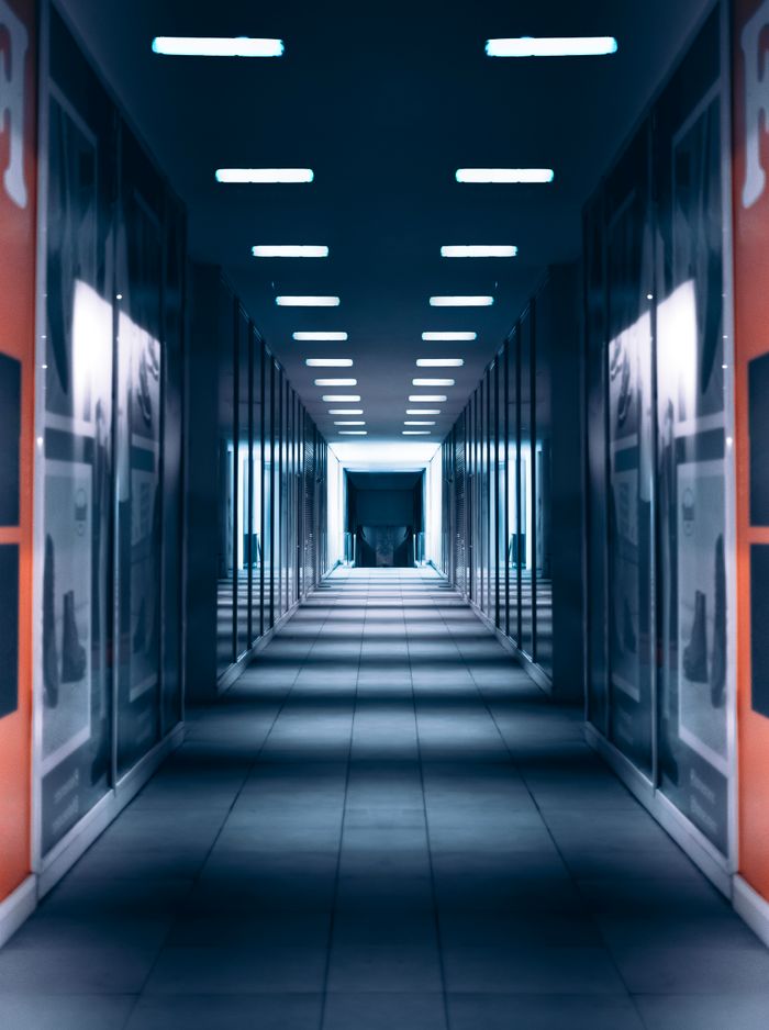 A long, empty corridor with blue lighting and reflective surfaces, offering a futuristic feel.